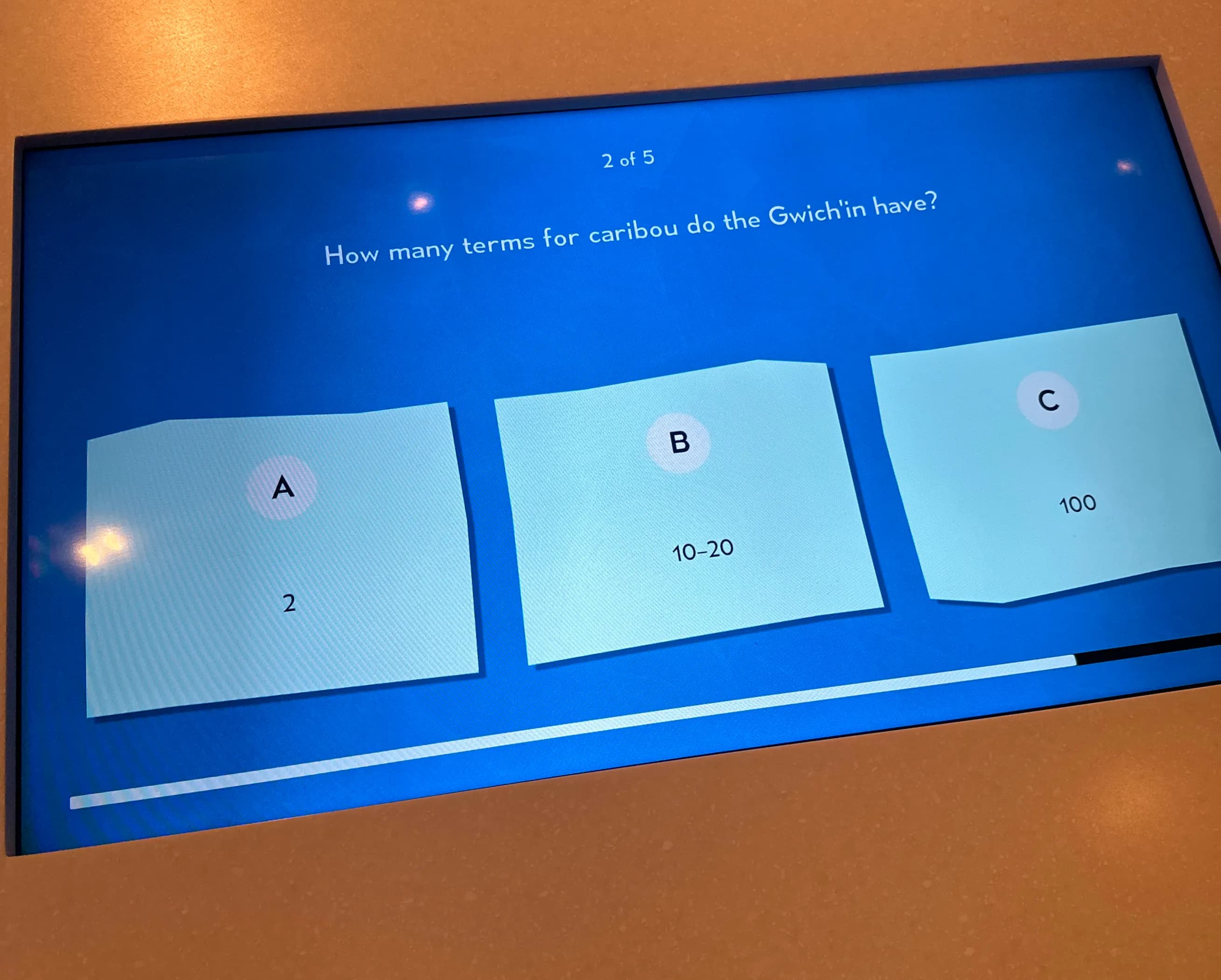 Interactive touchscreen quiz showing the question with answer cards and a progress indicator.